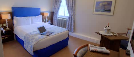 A hotel room with a bed, a desk, a chair, a lamp, a picture on the wall, and a window with curtains.