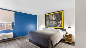 A modern hotel room with a bed, bedside lamps, a nightstand, and a large cityscape painting on the wall.
