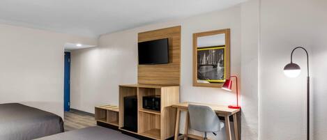 A hotel room with two beds, a desk with a chair, a television, a red desk lamp, and a floor lamp.
