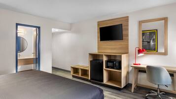 A hotel room with a bed, a desk with a computer, a TV, and a microwave.