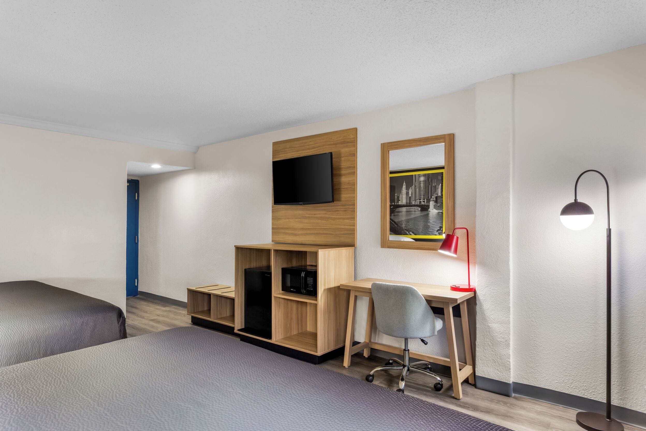Une chambre d’hôtel avec deux lits, un bureau avec une chaise, une télévision, un miroir et une lampe sur pied.