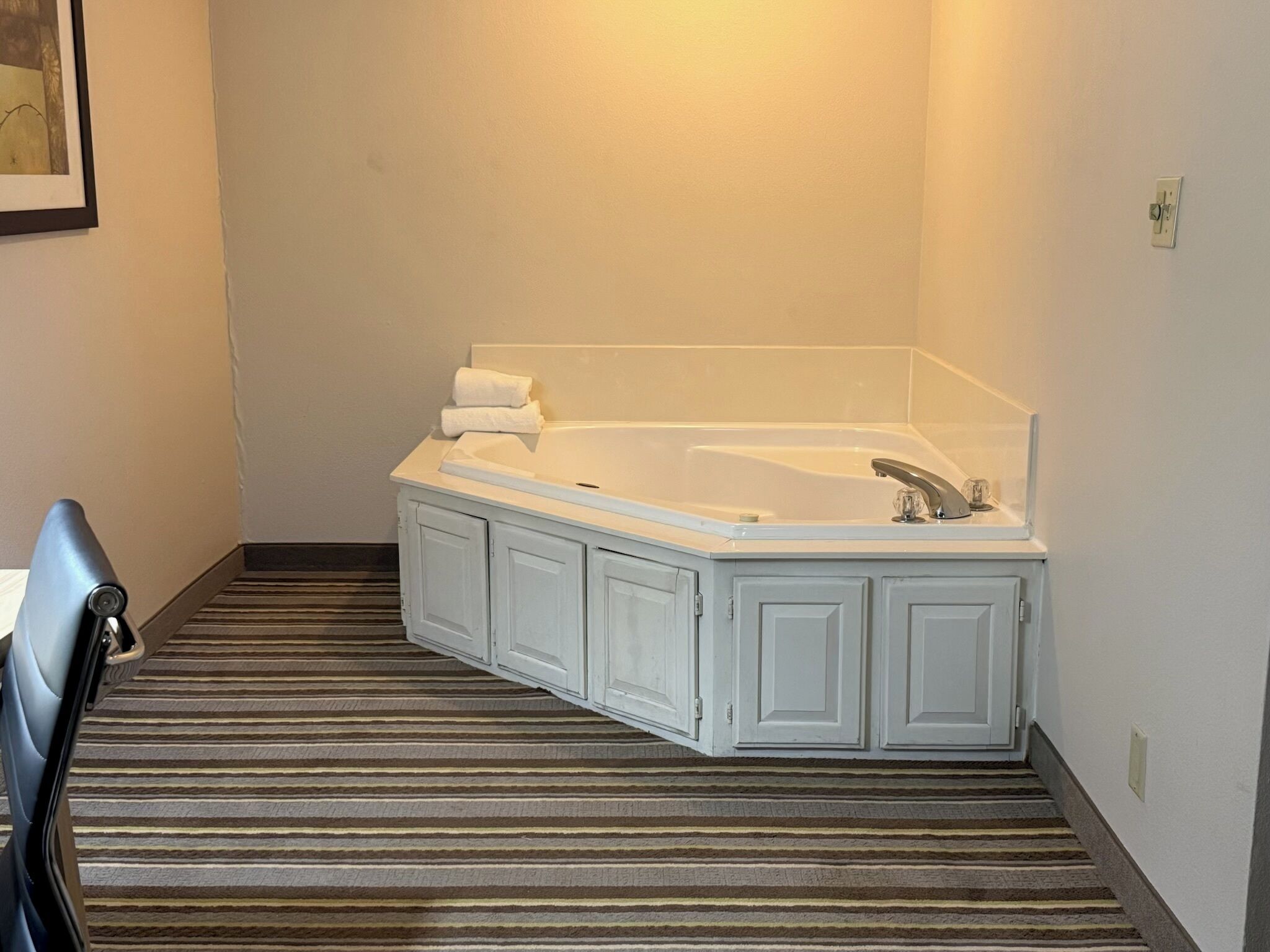 A bathroom with a bathtub, a towel rack, and a striped carpet.