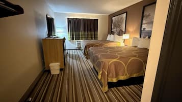 A hotel room with a bed, a desk, a chair, a trash bin, and a window with curtains.