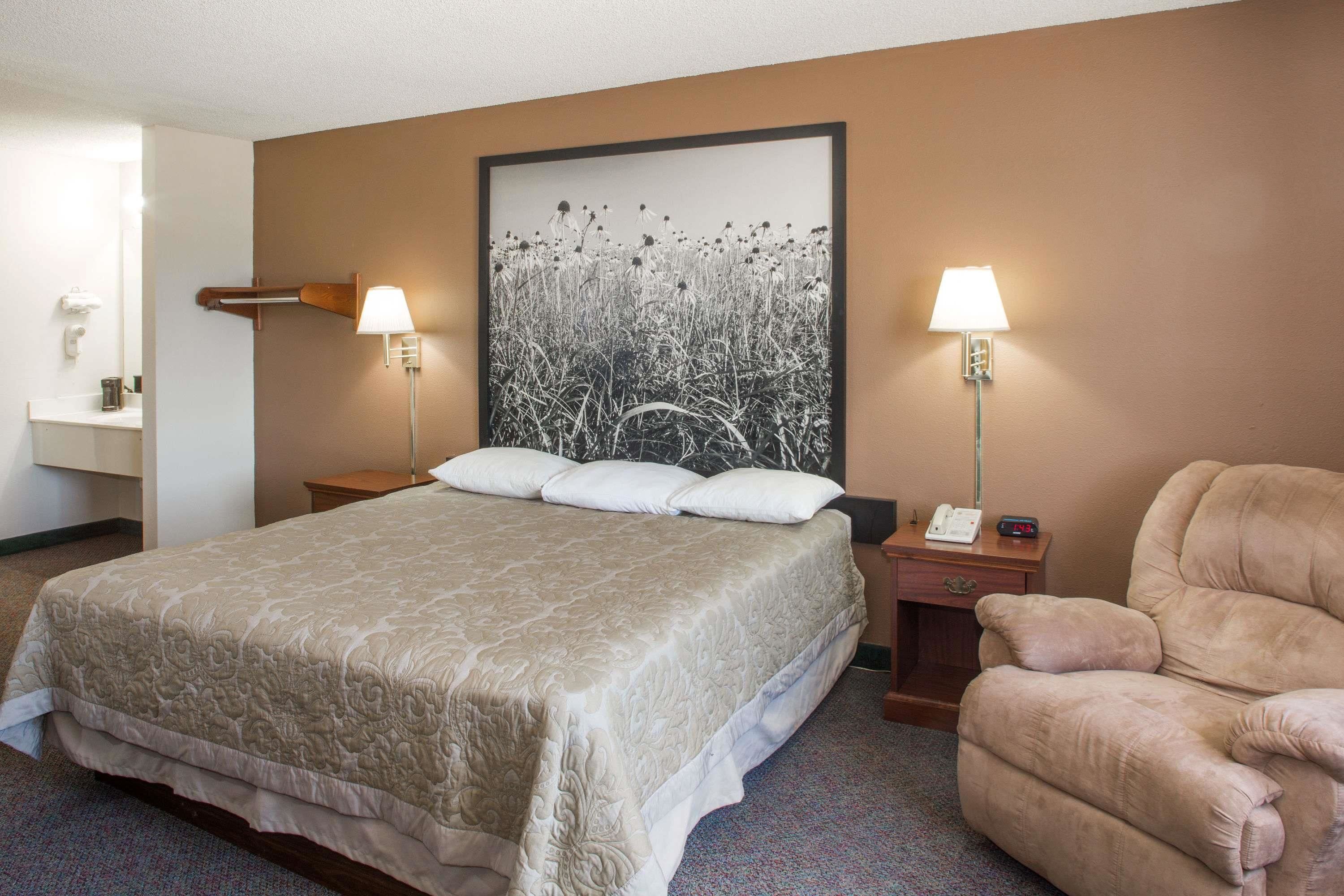Quarto de hotel com uma cama grande, duas mesas de cabeceira, uma cadeira e uma luminária na parede.