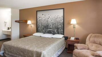 Quarto de hotel com uma cama grande, duas mesas de cabeceira, uma cadeira e uma luminária na parede.