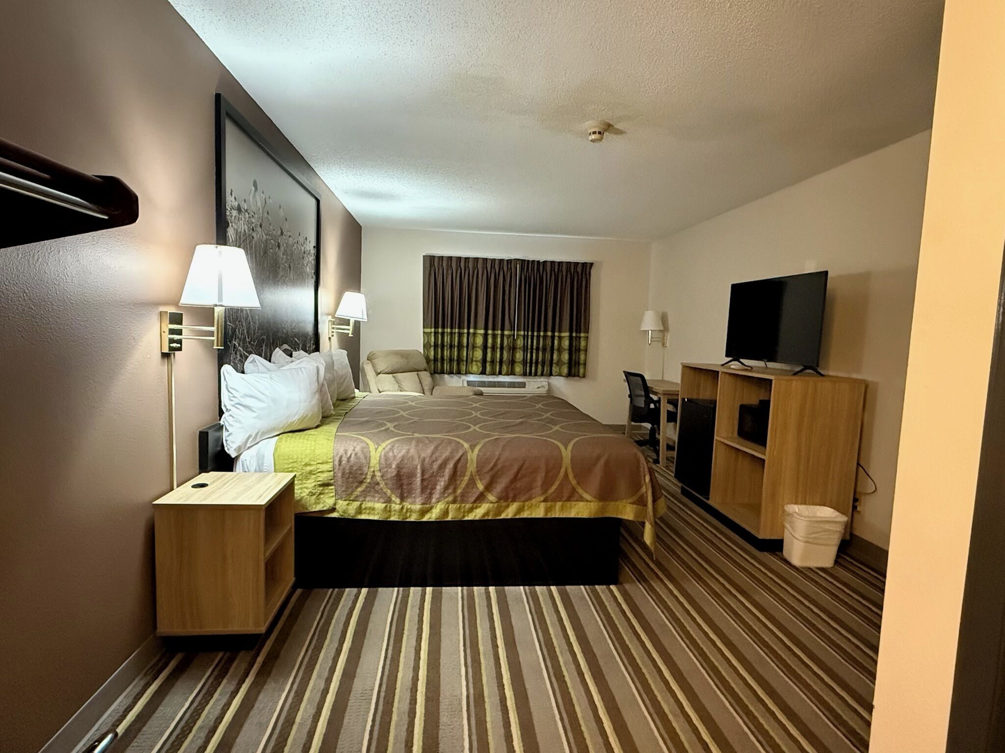 A hotel room with a bed, bedside tables, a TV, a desk, and a chair.