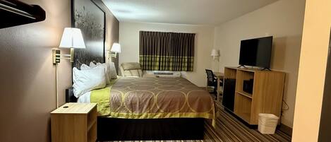 A hotel room with a bed, bedside tables, a TV, a desk, and a chair.