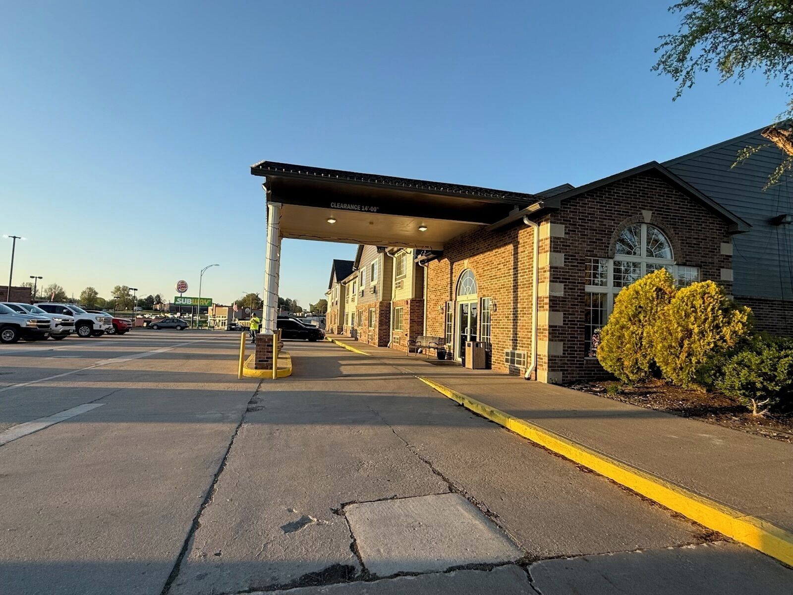 A parking lot with a building that has a covered entrance and a brick facade.