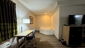 Une chambre d’hôtel comprenant un lit, un bureau avec une chaise, une télévision et une salle de bain avec une baignoire.