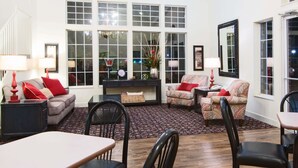Un salon spacieux avec une grande fenêtre, un canapé, deux fauteuils, une table à manger et un tapis.