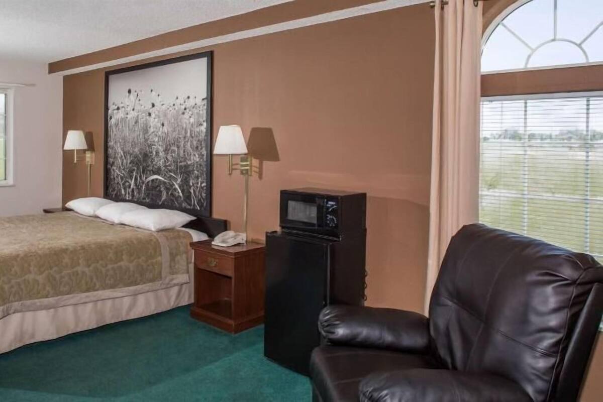 Habitación de hotel con cama, escritorio con teléfono, televisión, sillón de cuero y ventana grande.