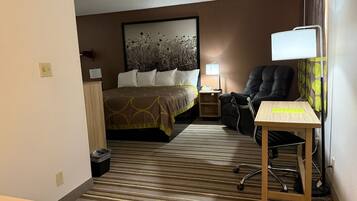 Quarto de hotel com cama, escrivaninha, cadeira, abajur e quadro na parede.