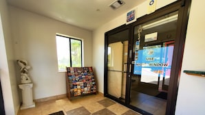 A hotel lobby with a reception desk, a bulletin board with various notices, a statue, and a window with a view of greenery.