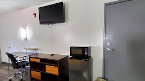 A small room with a desk, chair, microwave, refrigerator, trash can, and a closed door.