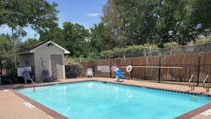 A rectangular swimming pool with a wooden deck surrounding it. There are two signs on the fence, one warning against diving and the other about no swimming on duty.