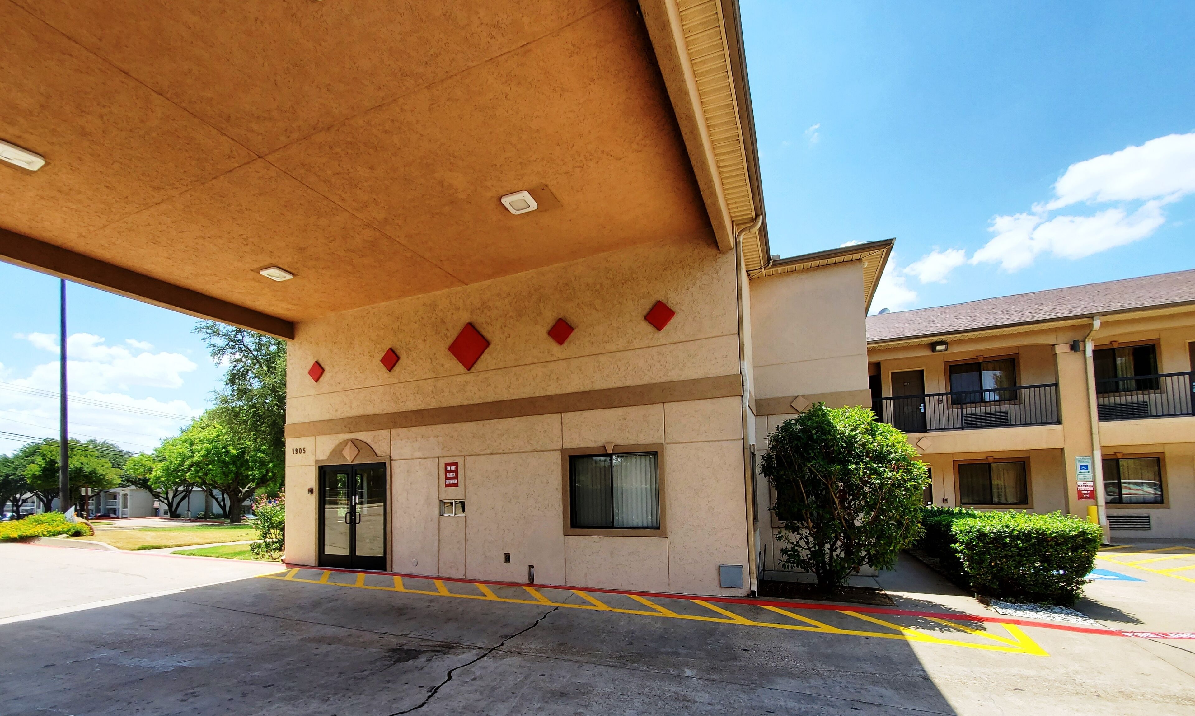 A building with a beige facade, a covered entrance, and a parking lot with marked spaces.