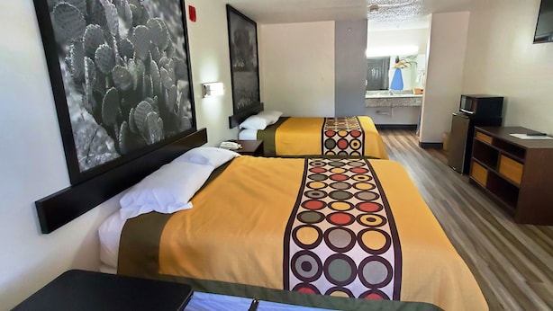 A hotel room with two beds, a desk, a TV, and artwork on the walls.