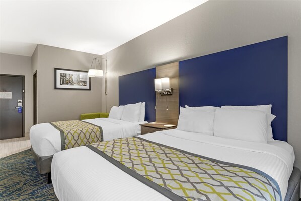 Habitación de hotel con dos camas, un escritorio y una silla. Se observa un cuadro en la pared y una puerta con cerradura.