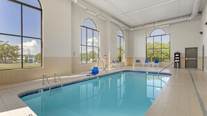 A large indoor swimming pool with clear blue water, surrounded by tiled walls and large windows.