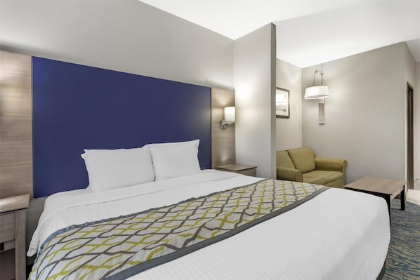 A hotel room with a large bed, a nightstand, a seating area with a chair, and a small table.