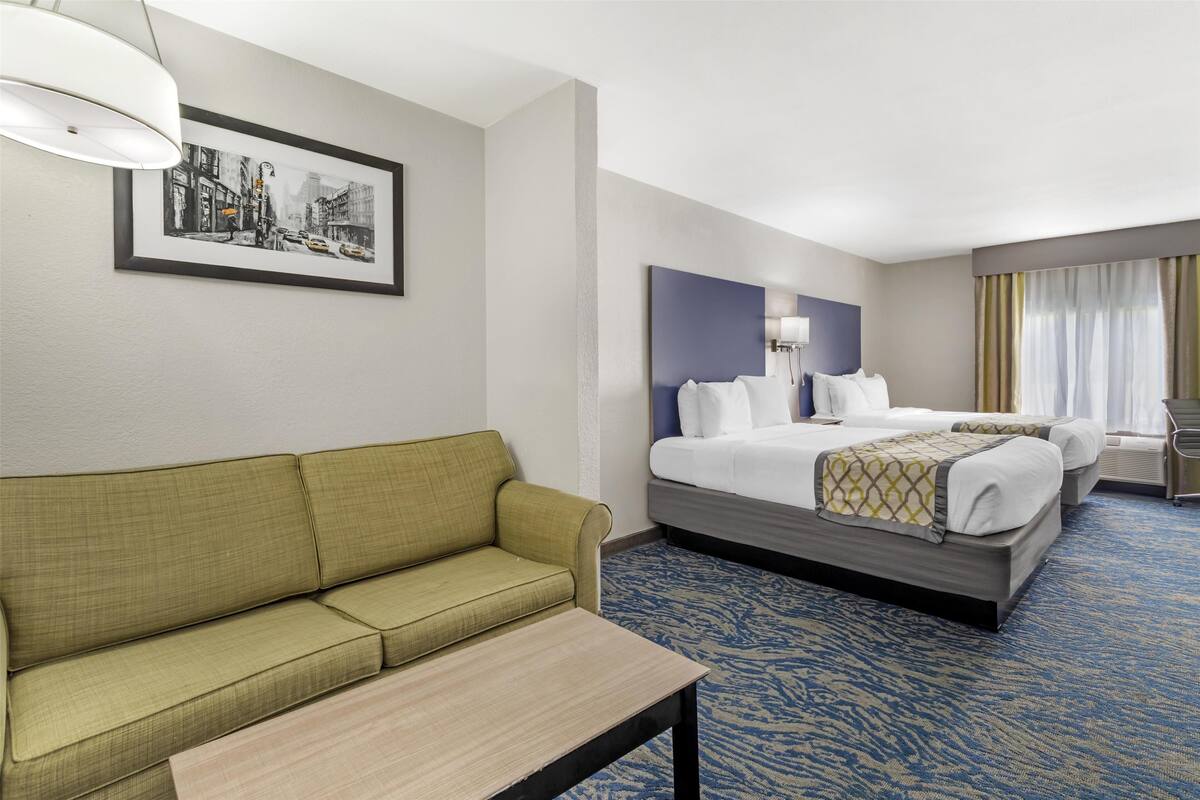 A hotel room with a green sofa, a bed with a headboard, a bedside table, and a framed cityscape picture on the wall.