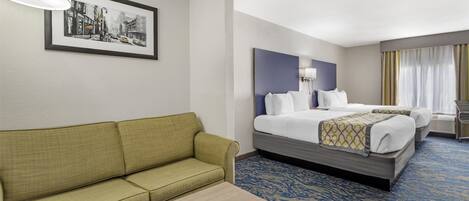 A hotel room with a green sofa, a bed with a headboard, a bedside table, and a framed cityscape picture on the wall.