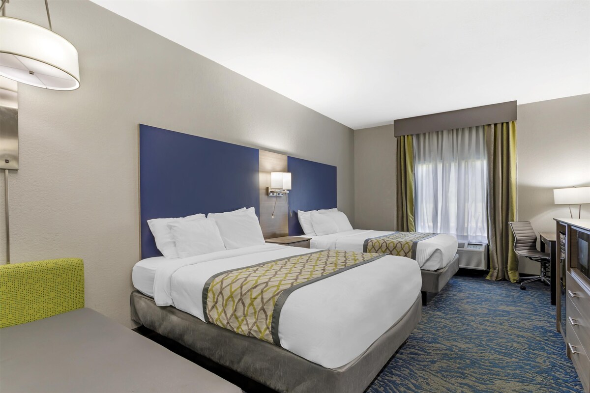 A hotel room with two beds, a desk, a chair, a TV, and a window with curtains.