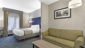 A hotel room with a bed, a sofa, a table, a lamp, and a framed picture on the wall.