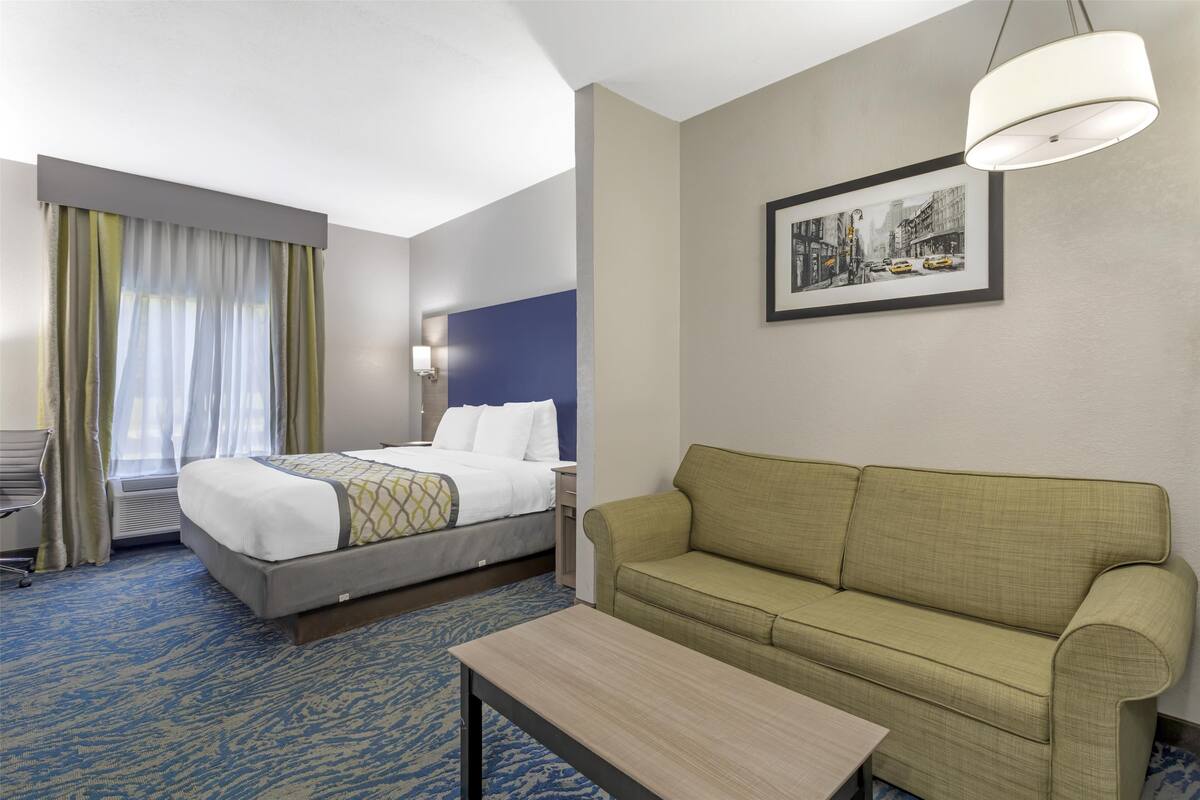 A hotel room with a bed, a sofa, a table, a lamp, and a framed picture on the wall.