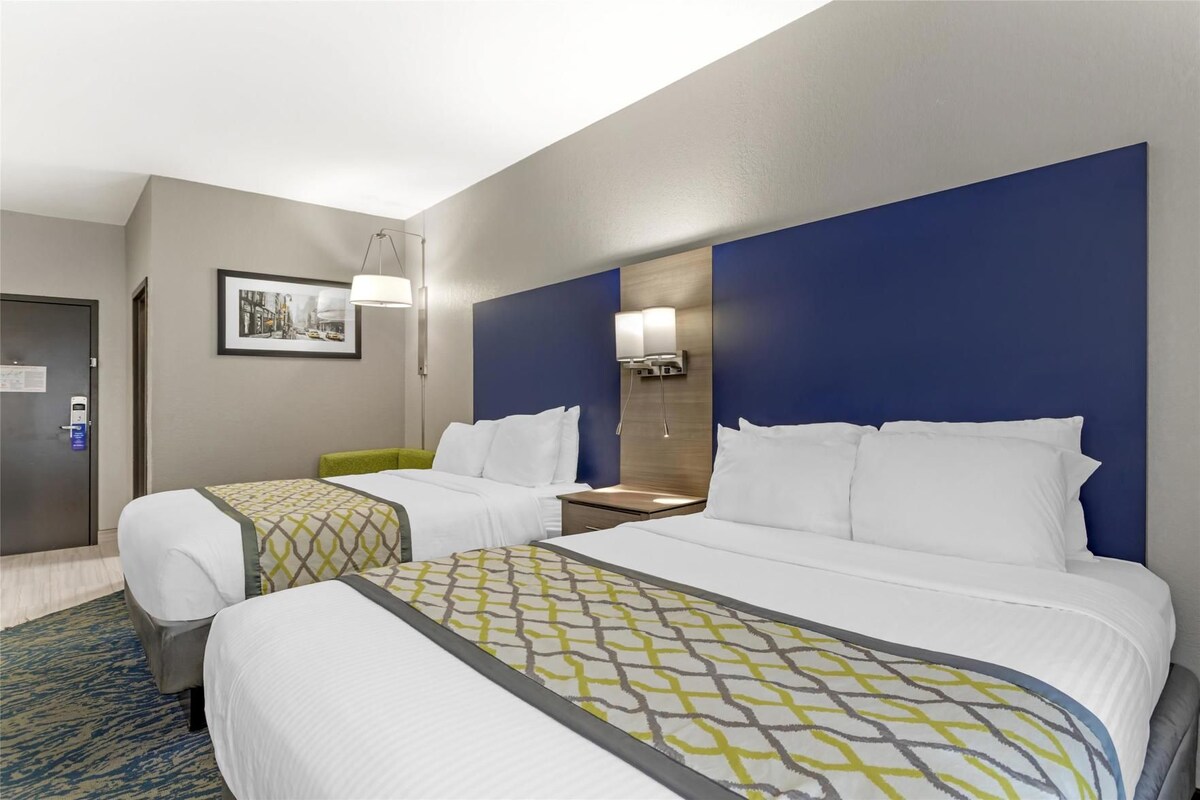 A hotel room with two beds, a desk, a chair, a lamp, and a framed picture on the wall.