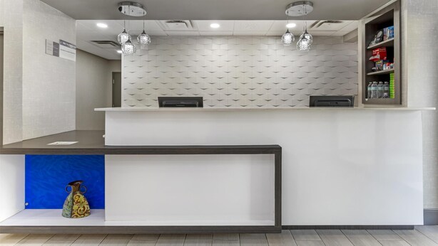 A reception area with a white reception desk, two pendant lights, a blue shelf with a vase, and a wall-mounted shelf with various items. - Best Western Knoxville Airport/Alcoa (Alcoa)