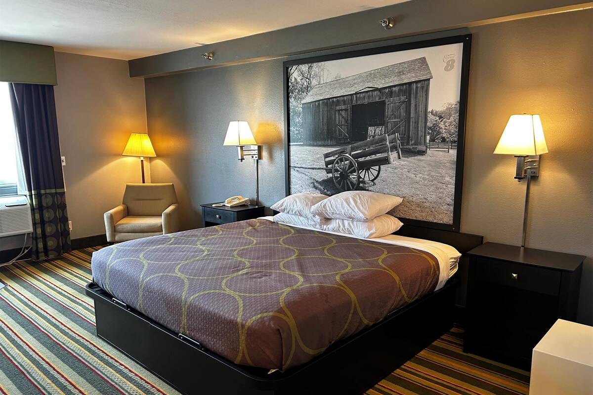 Een hotelkamer met een groot bed, twee bedlampen, een stoel, een bureau en een aan de muur bevestigde telefoon.