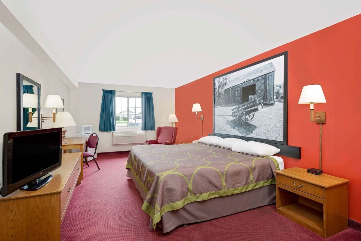Une chambre d’hôtel avec un lit, un bureau équipé d’un ordinateur, une télévision et une grande fenêtre avec des rideaux.