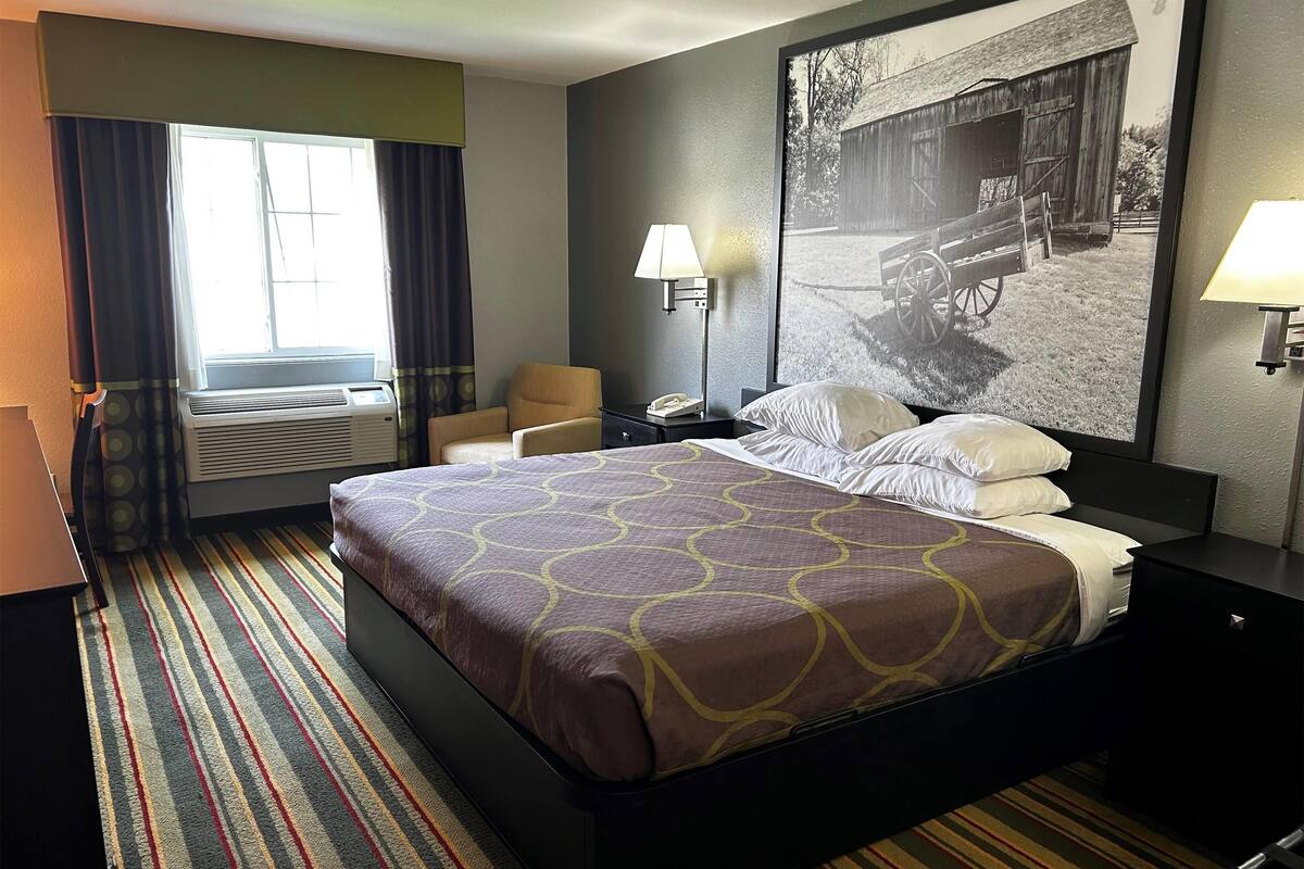 Een hotelkamer met een groot bed, een stoel, een bureau, een lamp en een raam met gordijnen.