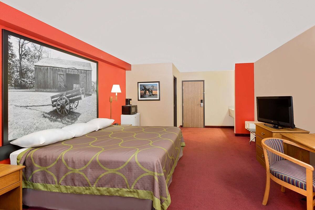 Een hotelkamer met een bed, een bureau met een televisie, een stoel, een lamp en een schilderij aan de muur.