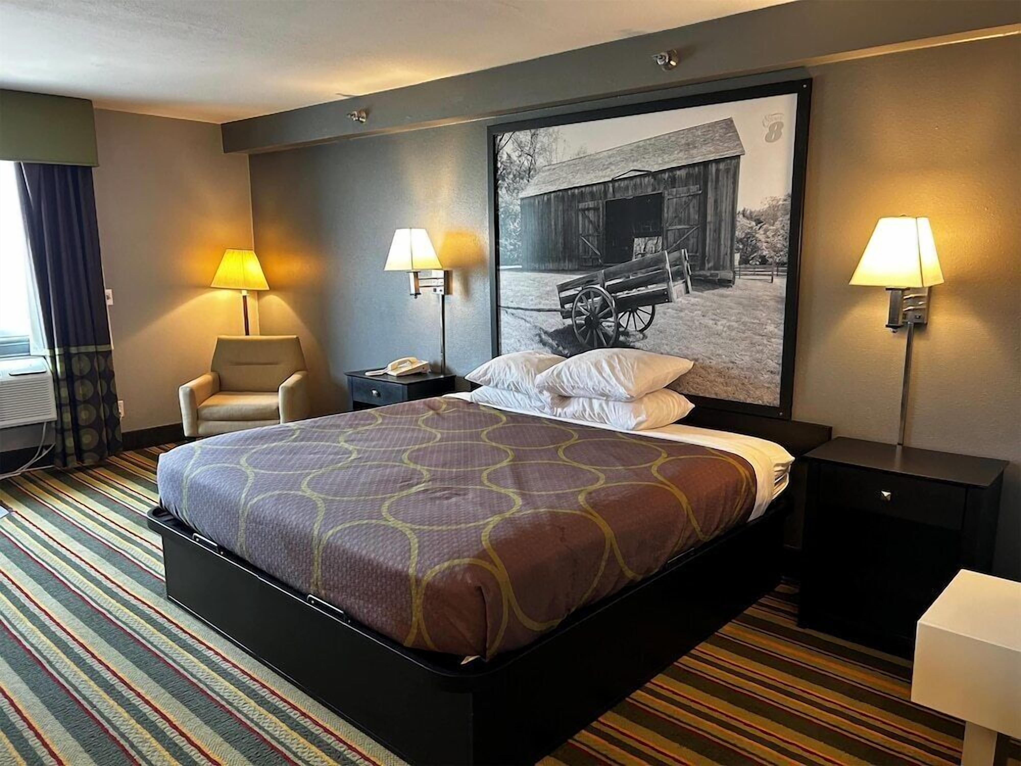 Une chambre d’hôtel avec un grand lit, deux lampes de chevet, une chaise, une table de chevet et un téléviseur fixé au mur.