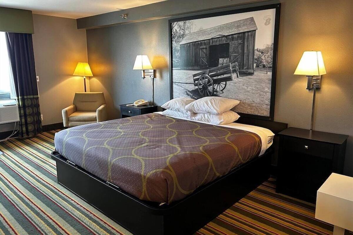 Een hotelkamer met een groot bed, twee bedlampen, een stoel, een nachtkastje en een aan de muur bevestigde televisie.