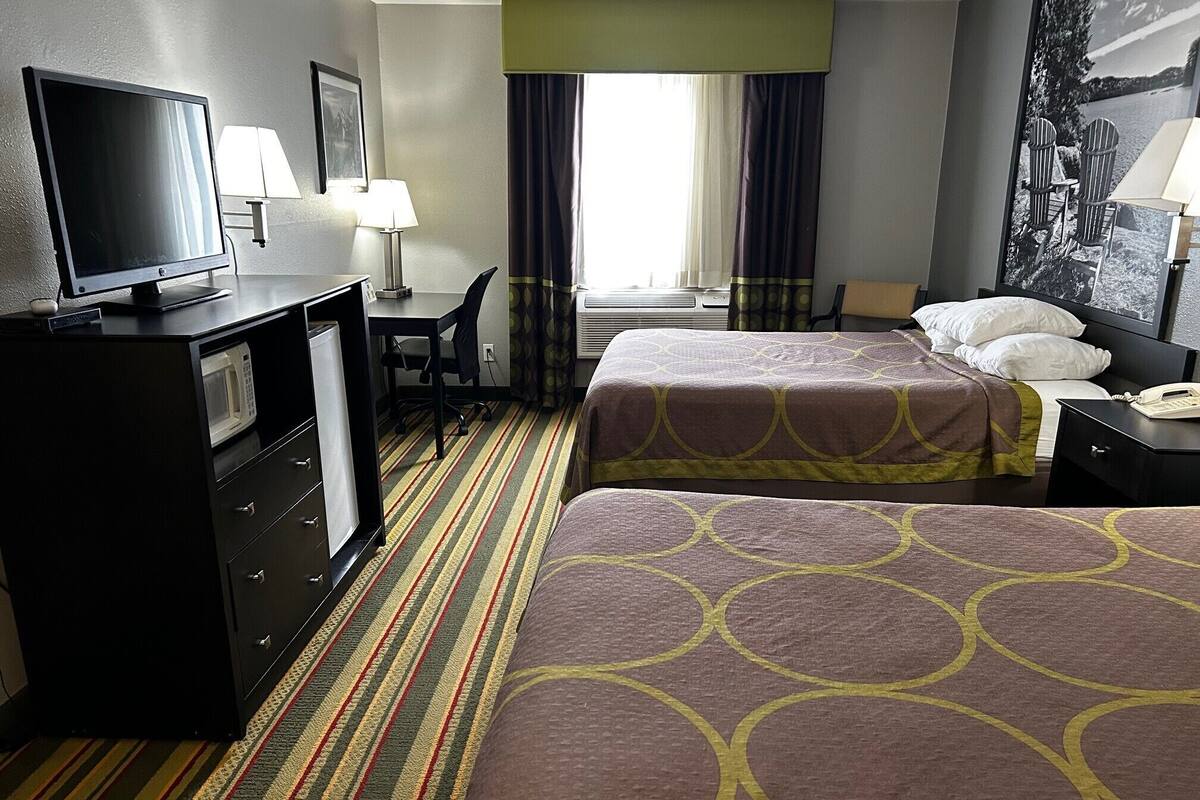 Een hotelkamer met een bed, een bureau, een televisie, een lamp en een raam met gordijnen.