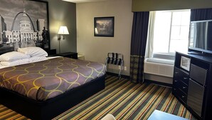 Hotellihuone, jossa on suuri sänky, työpöytä tuolilla, televisio, ikkuna verhoilla, taulu seinällä ja lamppu.