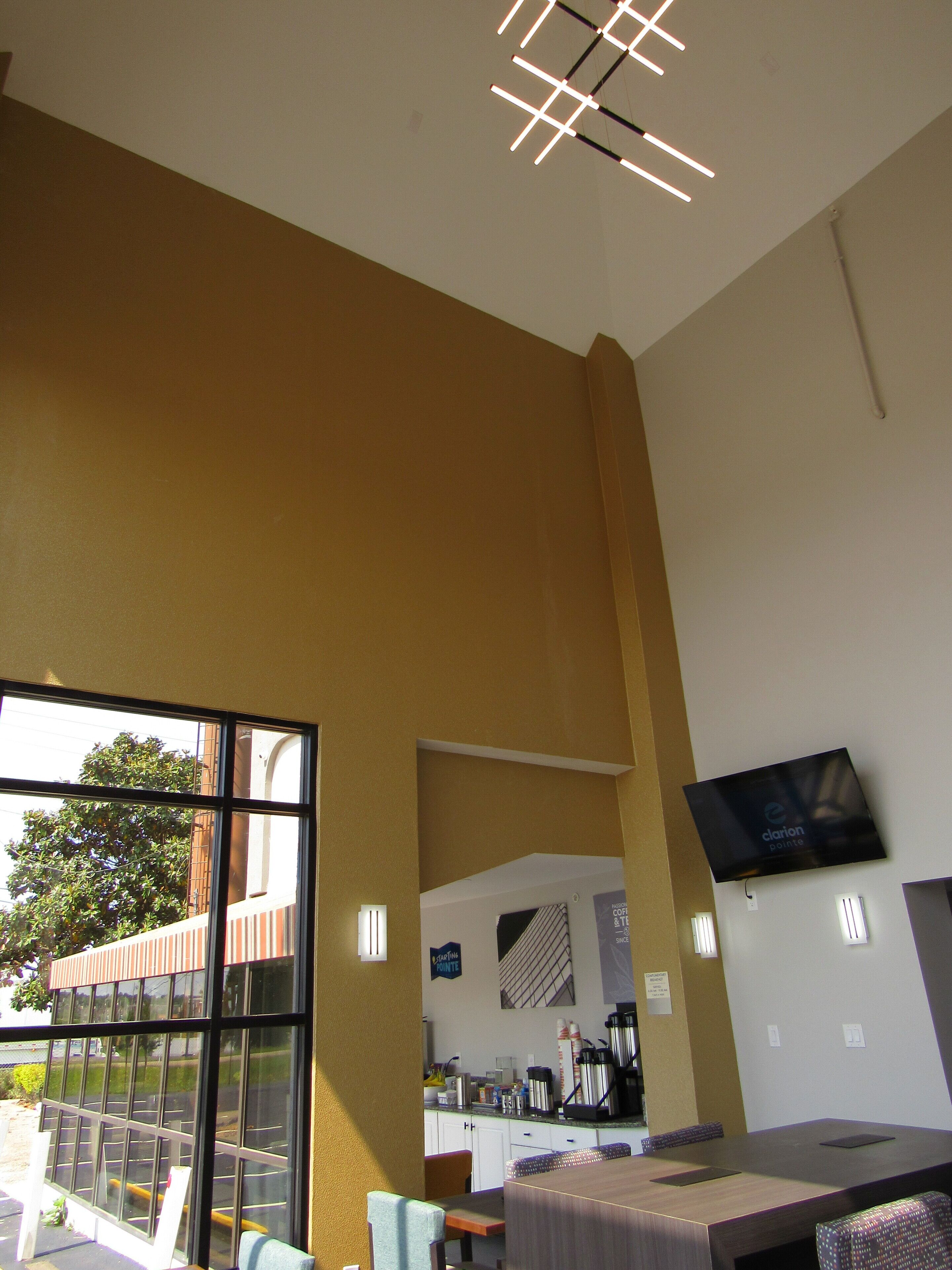 A modern hotel room with a large window, a flat-screen TV mounted on the wall, and a wooden table.
