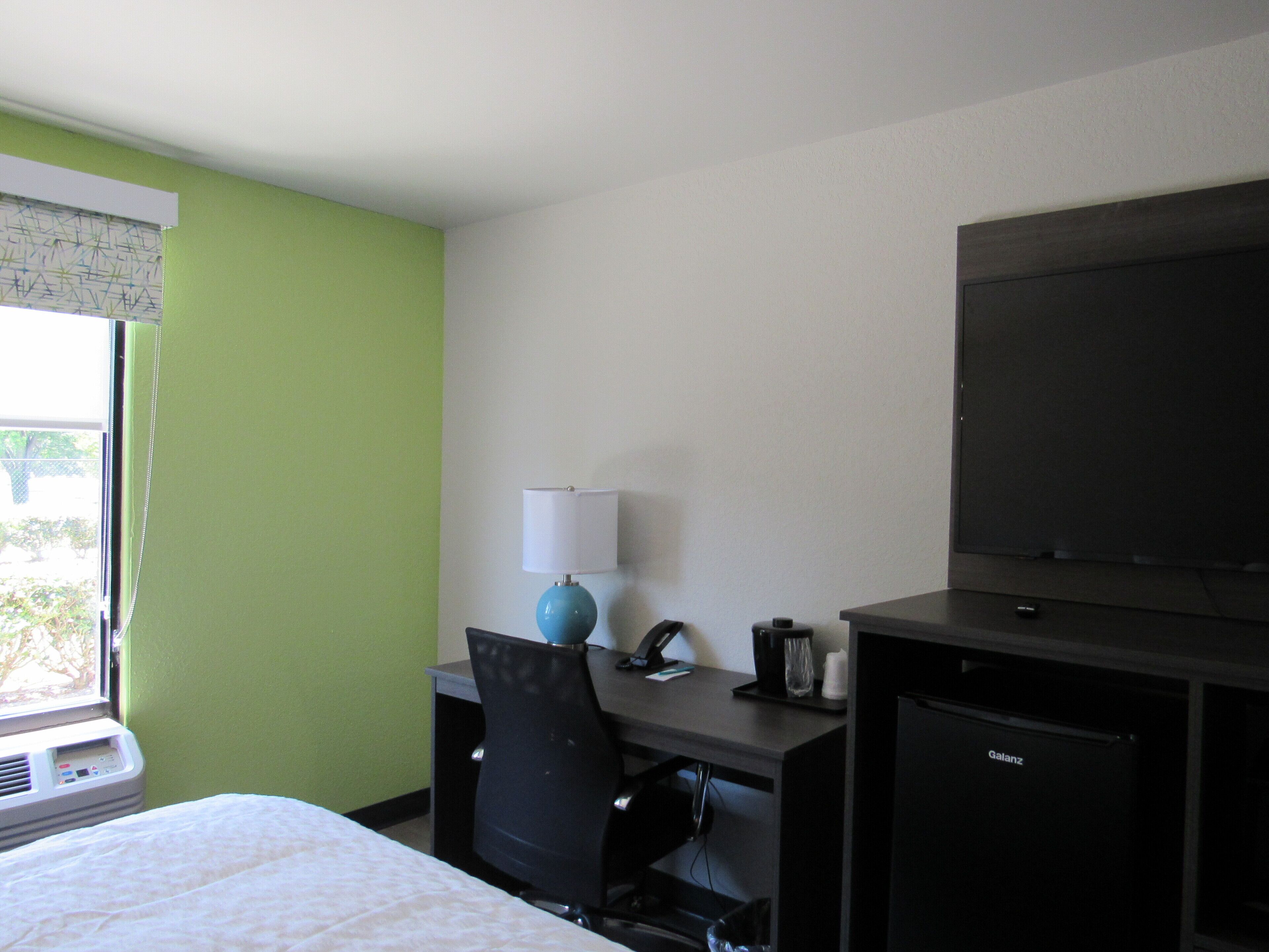 Ein Hotelzimmer mit einem Bett, einem Schreibtisch mit Lampe, einem Sessel, einem Fernseher und einer Minibar.