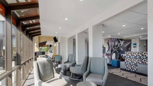 A modern lobby with seating areas, a large mural, and a view through glass walls. - Clarion Pointe McDonough (McDonough)