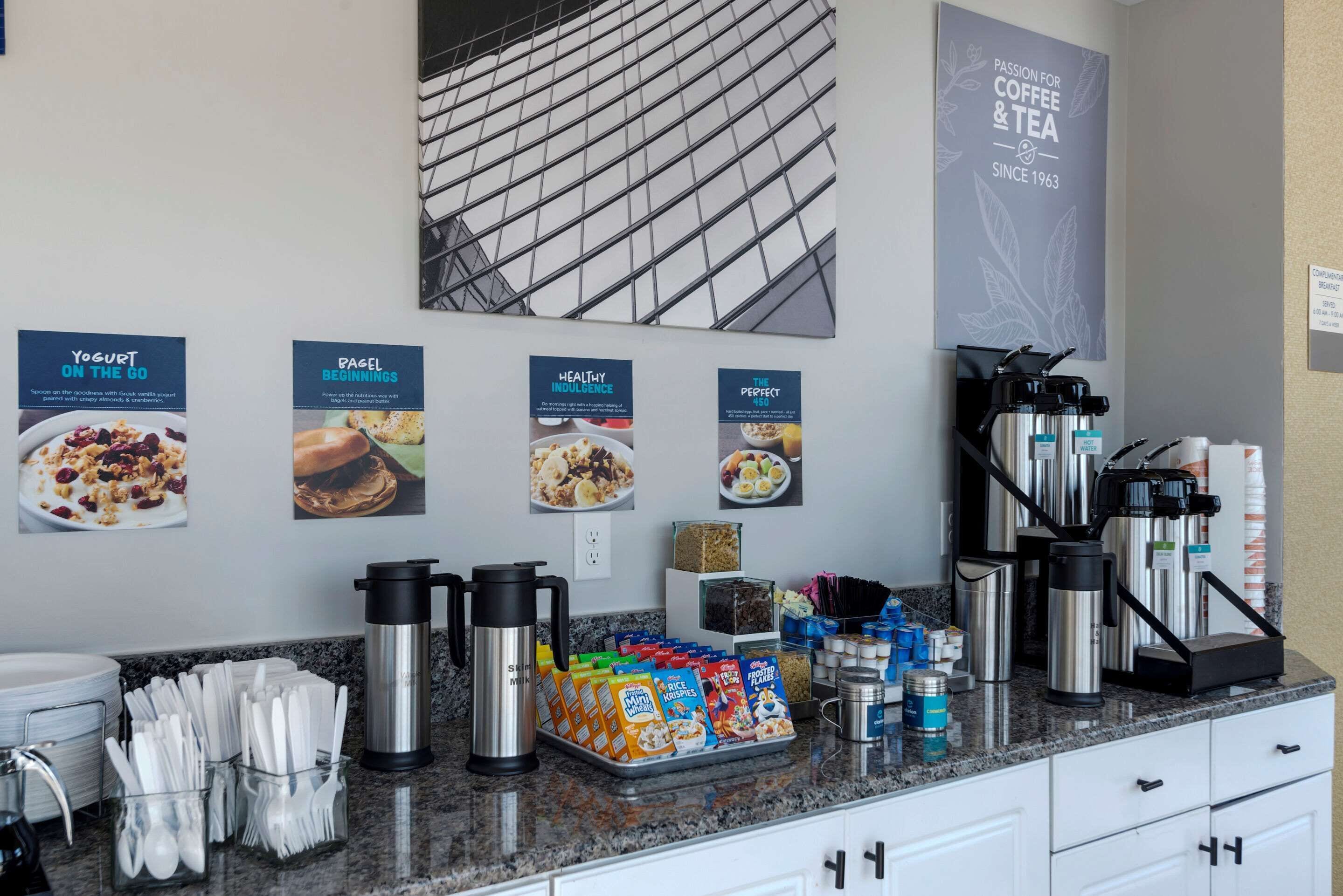 A modern kitchen area with a coffee station, including a coffee maker, milk frother, and various coffee pods. There are also condiments and utensils neatly arranged on the counter.
