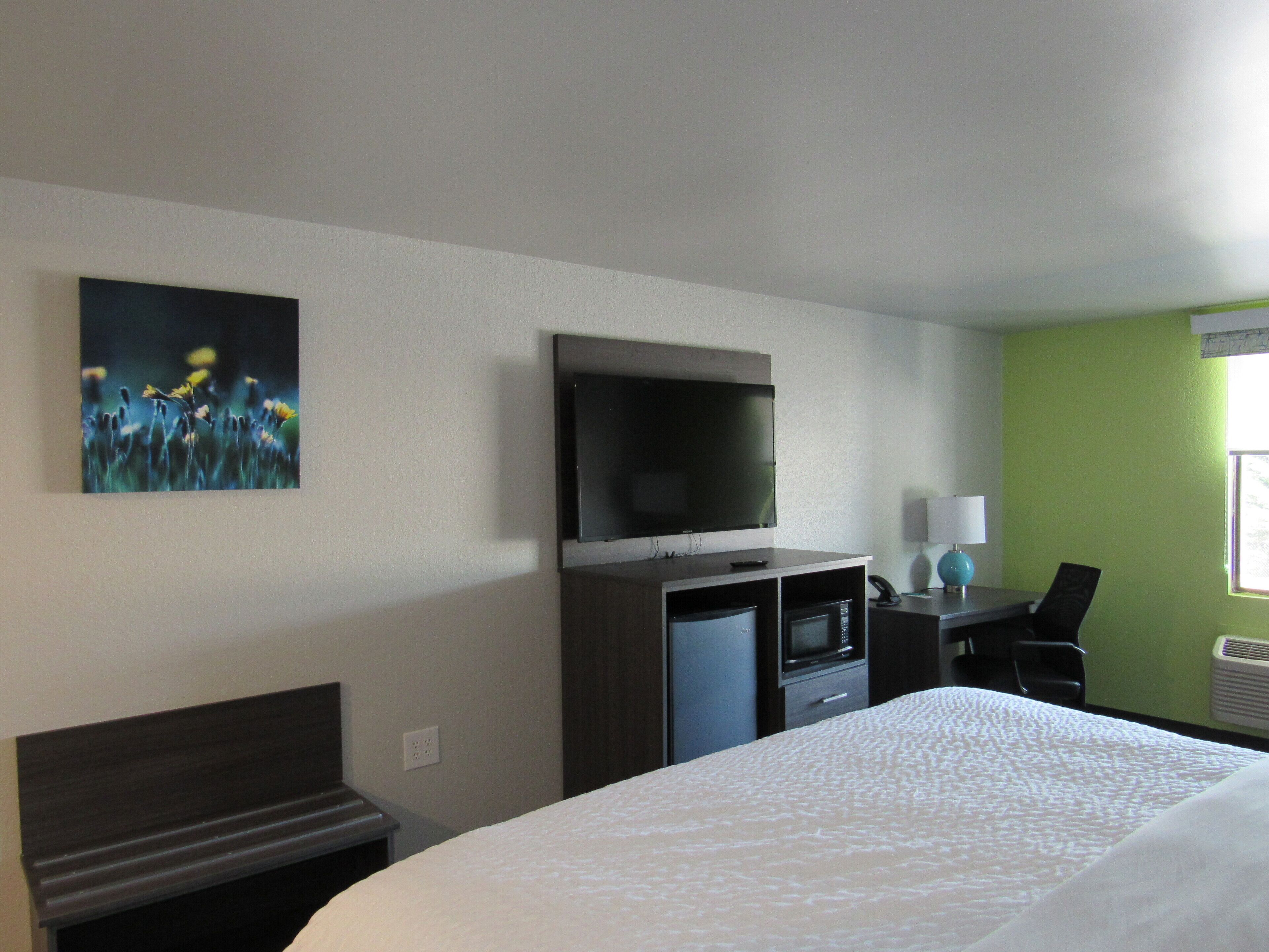 A hotel room with a bed, a TV mounted on the wall, a desk with a lamp, and a painting on the wall.