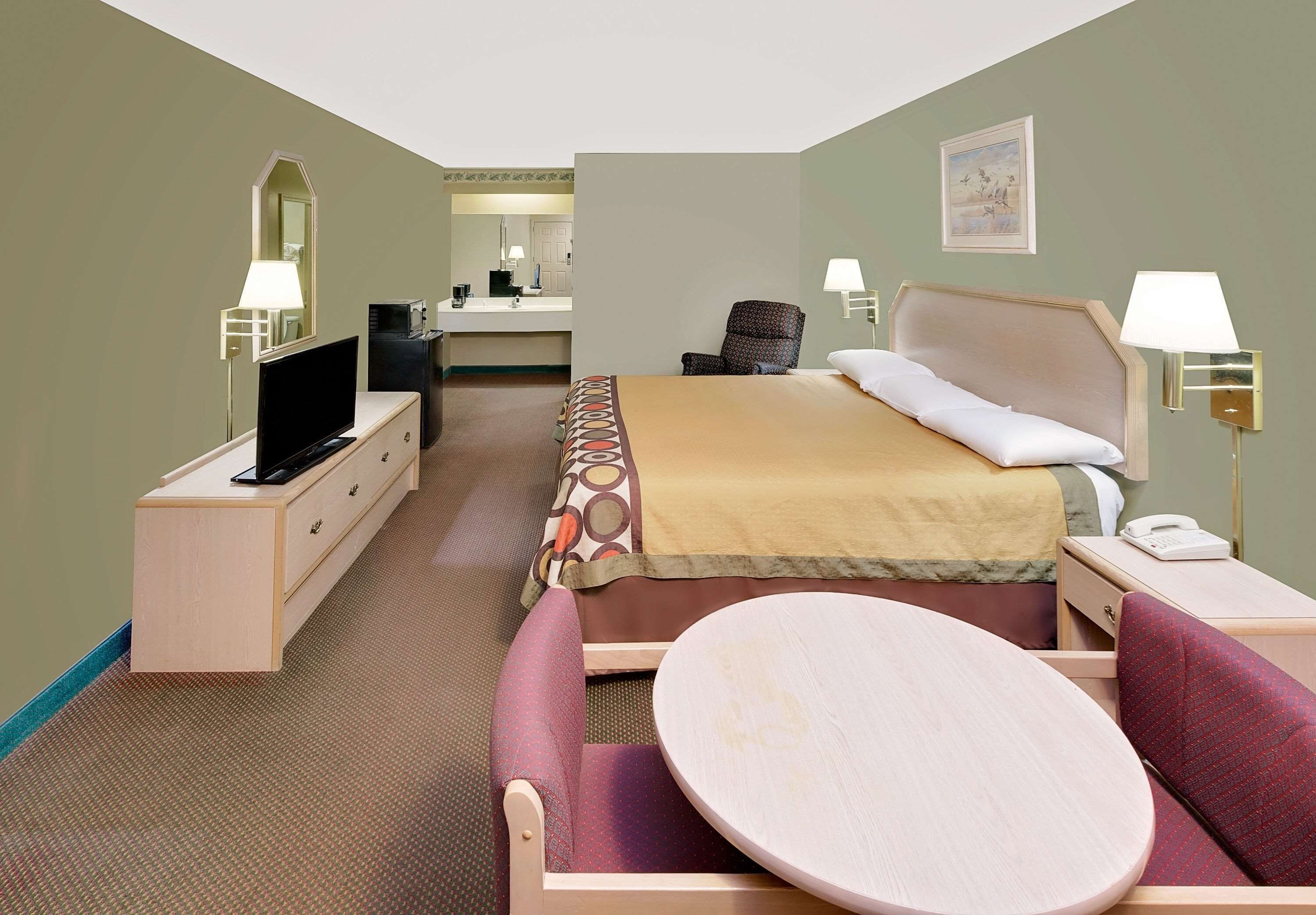 A hotel room with a bed, a desk with a computer, a chair, a round table, and a TV.