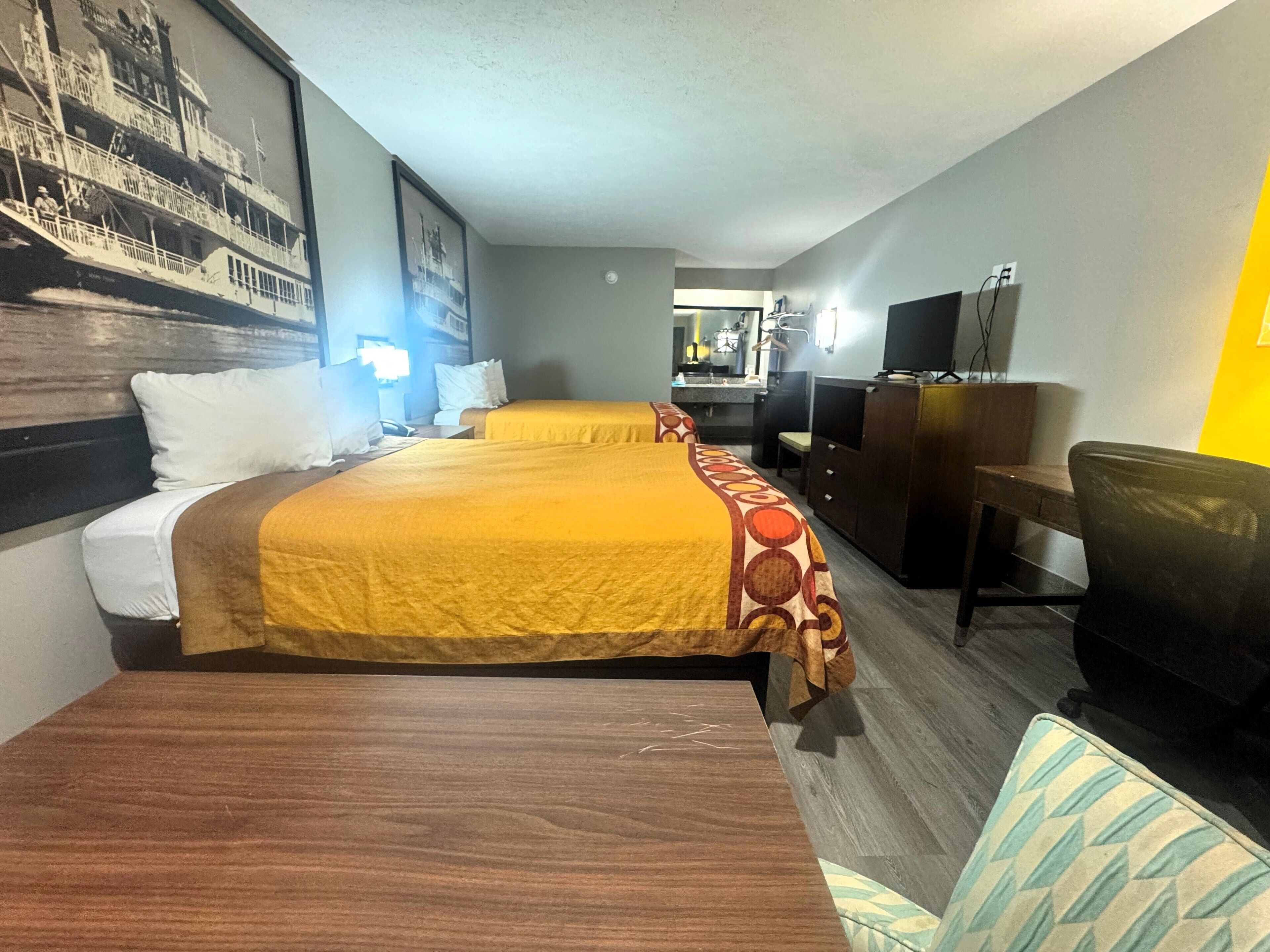 Habitación de hotel con dos camas, un escritorio, una silla, un televisor y un baño a la vista.