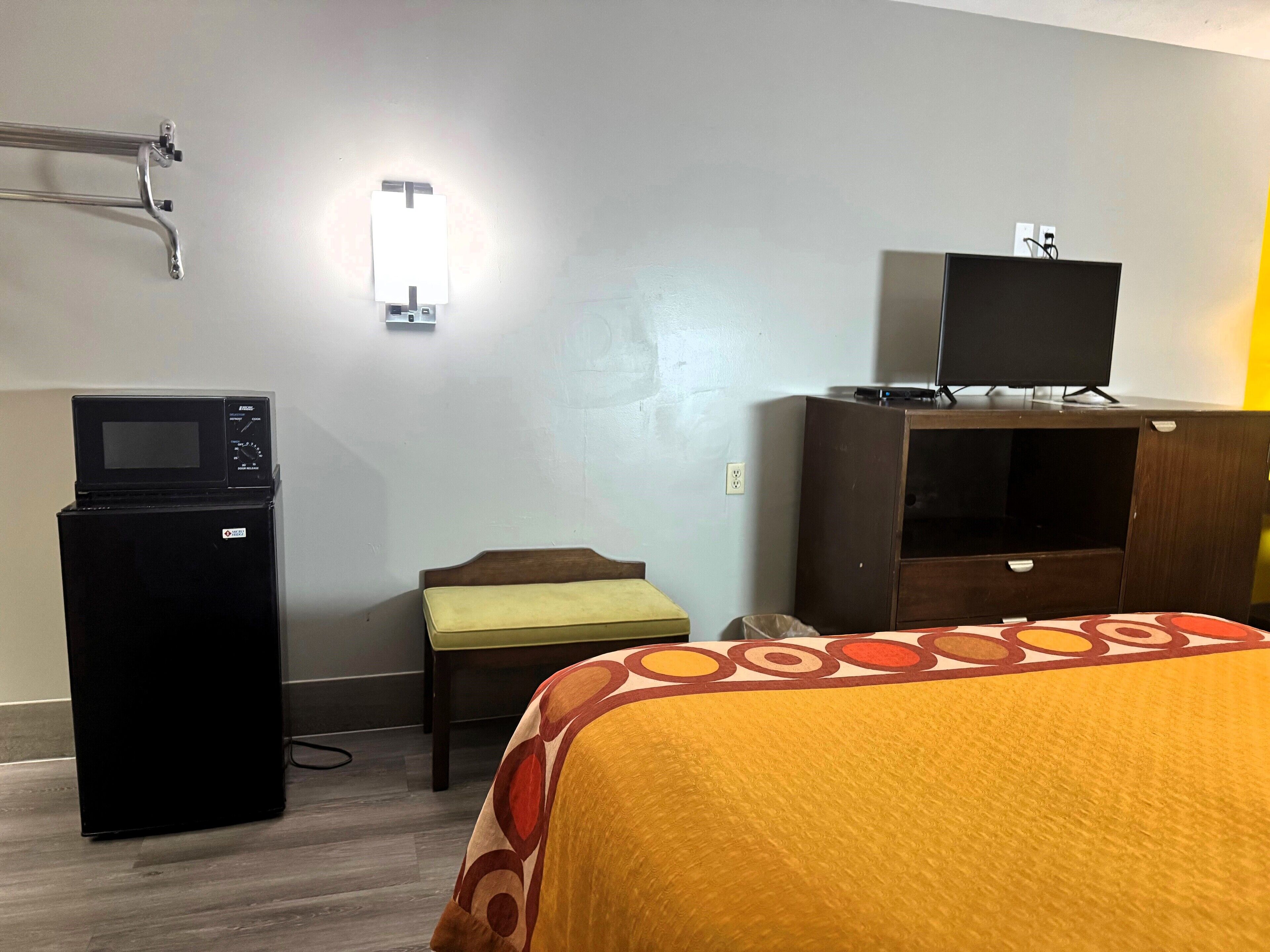 A hotel room with a bed, a desk with a microwave, a television on a cabinet, and a wall-mounted light.