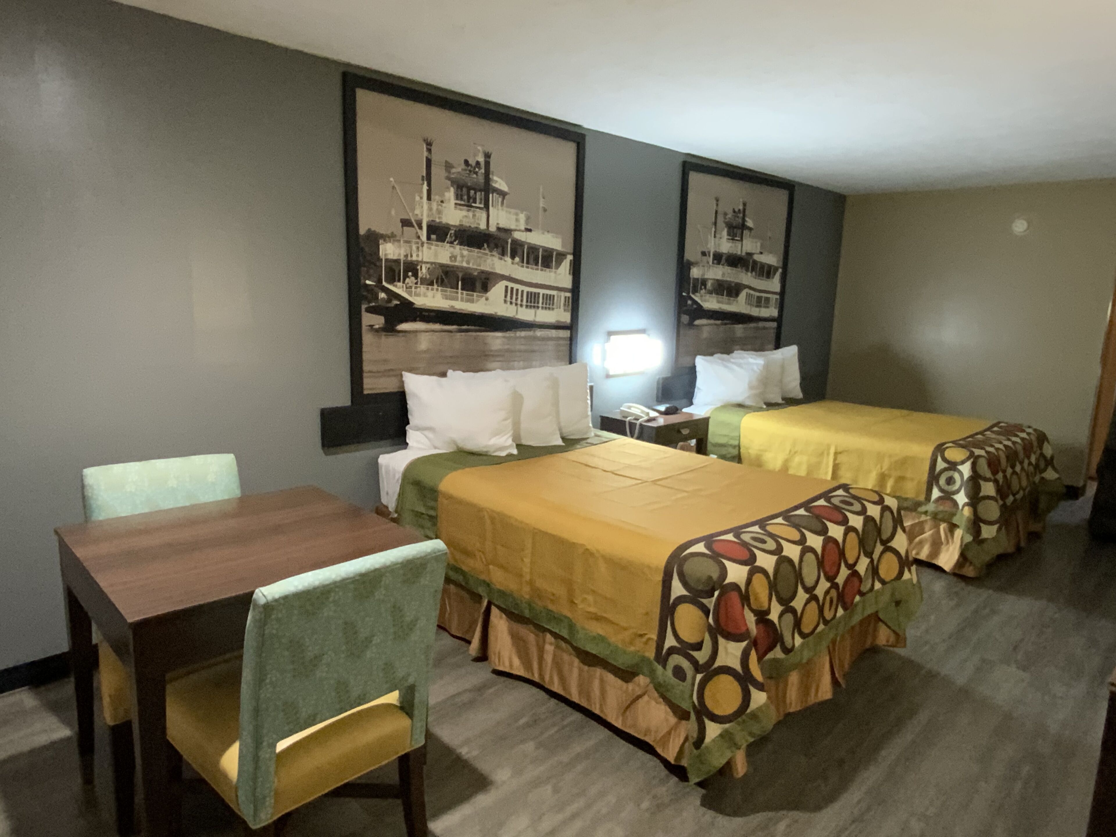 A hotel room with two beds, a desk, and a chair. There are two framed pictures on the wall.