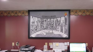 Een bureau met een lijst waarop een stadsbeeld staat, een computer en diverse kantoorbenodigdheden.