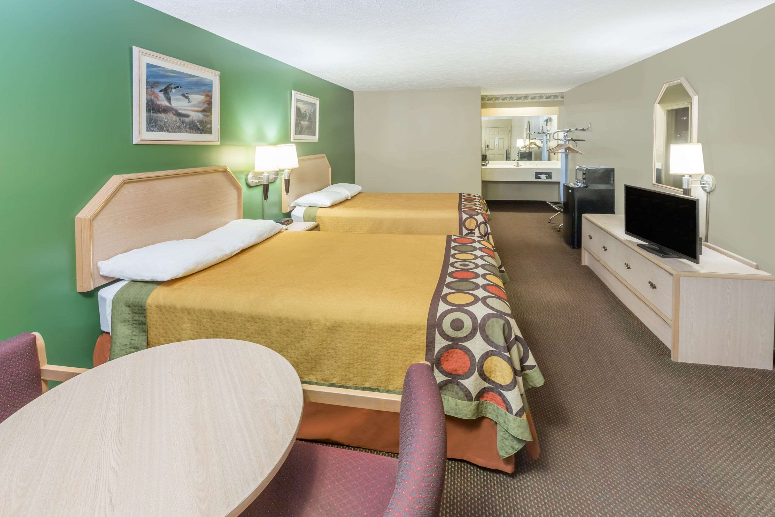 A hotel room with two beds, a desk, a chair, a television, a mirror, and a bathroom visible in the background.